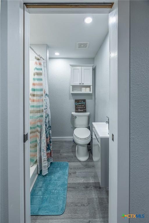 143 S Quailrun Ave, Port Lavaca, TX 77979 - full bathroom featuring wood finished floors, a shower with curtain, toilet, baseboards, and vanity