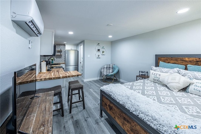 143 S Quailrun Ave, Port Lavaca, TX 77979 - bedroom with stainless steel fridge, a wall mounted air conditioner, wood finished floors, recessed lighting, and baseboards