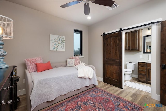 bedroom featuring ceiling fan, a barn door, connected bathroom, and light hardwood / wood-style floors