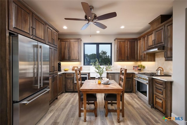 kitchen with high end appliances, dark brown cabinets, and light hardwood / wood-style flooring