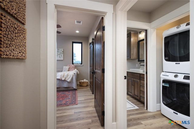 laundry area with sink, light wood-type flooring, a barn door, and stacked washing maching and dryer