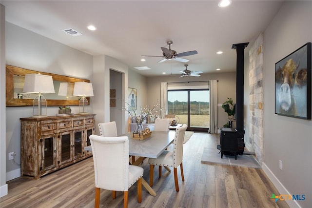 dining area featuring ceiling fan, a wood stove, and light hardwood / wood-style floors