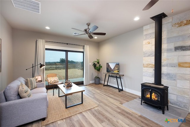 living room featuring ceiling fan, a wood stove, and light wood-type flooring