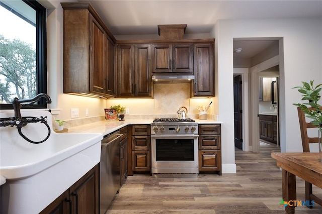 kitchen with appliances with stainless steel finishes, sink, dark brown cabinetry, and light hardwood / wood-style flooring