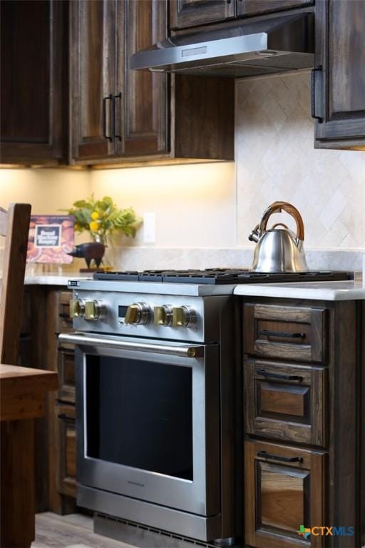 kitchen featuring high end stainless steel range oven, dark brown cabinets, and backsplash