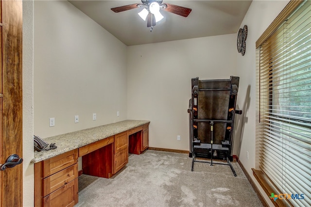 carpeted office space featuring built in desk, ceiling fan, and plenty of natural light