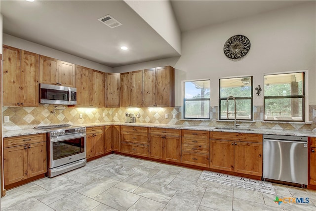 kitchen featuring tasteful backsplash, stainless steel appliances, high vaulted ceiling, light stone countertops, and sink