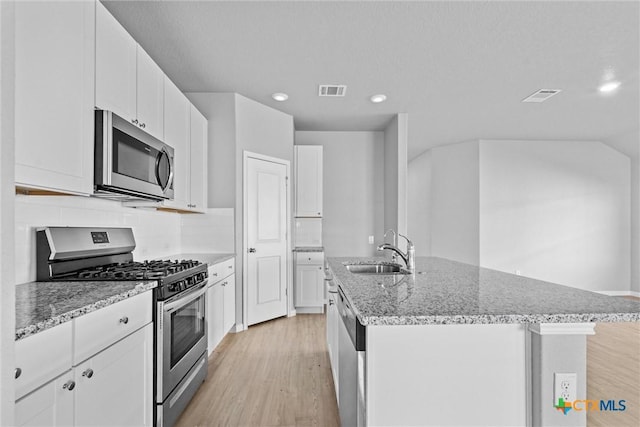 9063 Rancher Trl, Seguin, TX 78155 - kitchen with appliances with stainless steel finishes, a sink, light wood-style flooring, a kitchen island with sink, and light stone countertops