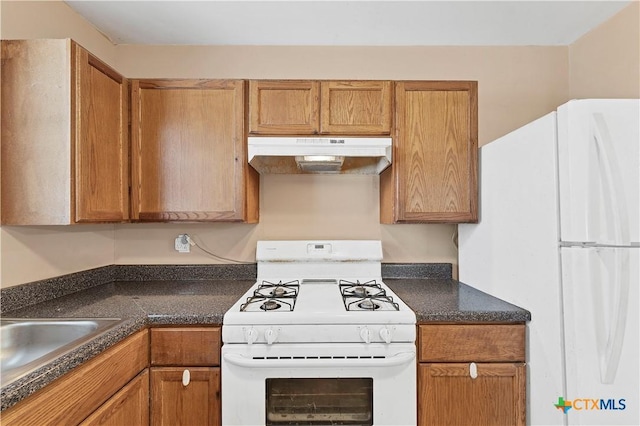 kitchen with white appliances, dark countertops, brown cabinets, and under cabinet range hood