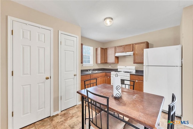 kitchen featuring white appliances, dark countertops, under cabinet range hood, and a sink