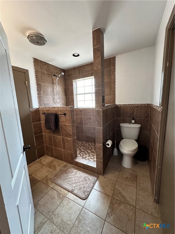 bathroom featuring a tile shower, tile patterned floors, tile walls, and toilet