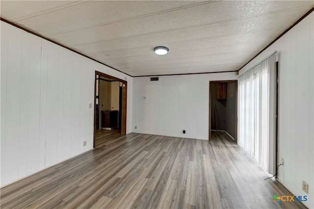 unfurnished room featuring wood walls, hardwood / wood-style floors, and ornamental molding