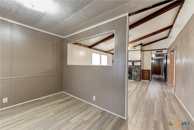 empty room with vaulted ceiling with beams, a stone fireplace, light wood-type flooring, and elevator