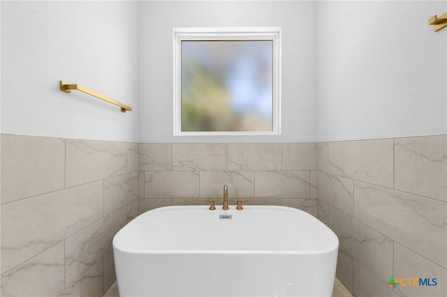bathroom featuring tile walls, a wainscoted wall, and a freestanding tub