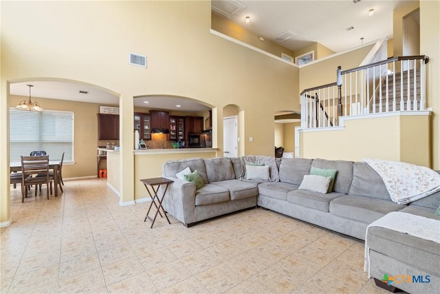 1002 Wallin Farms Cv, Hutto, TX 78634 - living room featuring a high ceiling, light tile patterned flooring, arched walkways, a chandelier, and stairs
