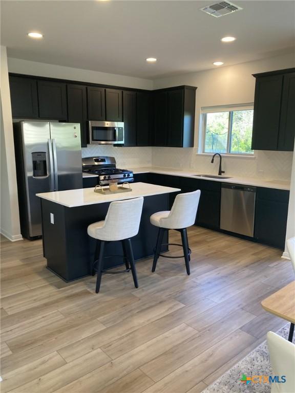 kitchen with dark cabinets, a kitchen island, visible vents, stainless steel appliances, and a sink