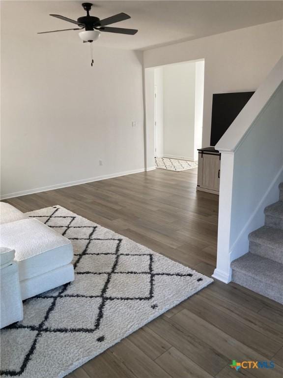 unfurnished living room with wood finished floors, baseboards, a ceiling fan, and stairs