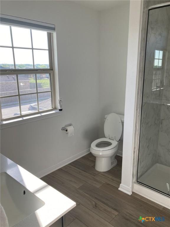 bathroom with toilet, baseboards, a marble finish shower, and wood finished floors