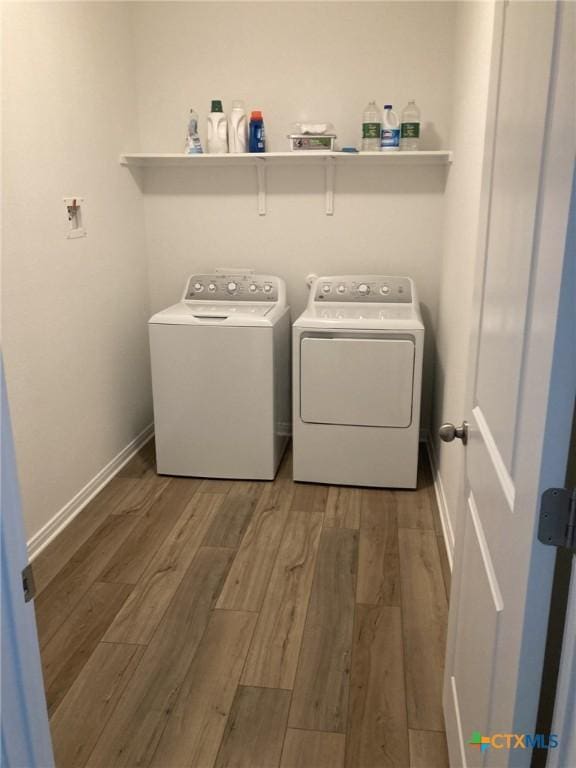 clothes washing area featuring washing machine and clothes dryer, wood finished floors, laundry area, and baseboards