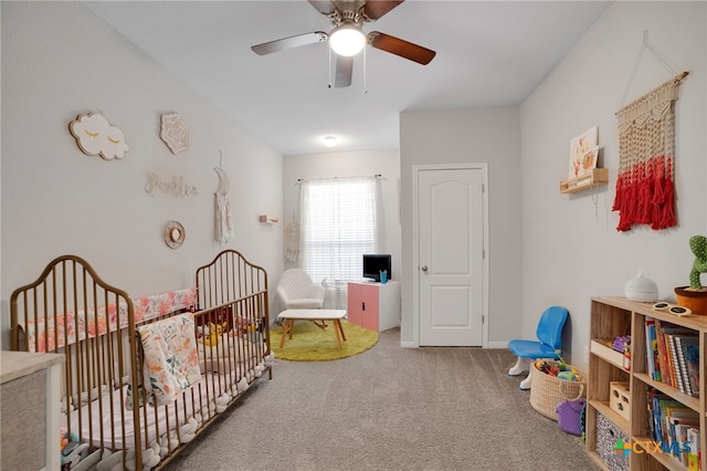 bedroom featuring a nursery area, carpet flooring, and ceiling fan