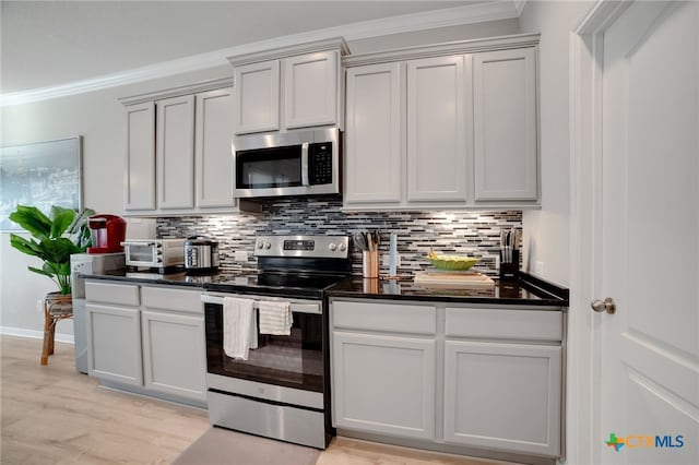 kitchen with stainless steel appliances, light hardwood / wood-style floors, dark stone counters, tasteful backsplash, and ornamental molding