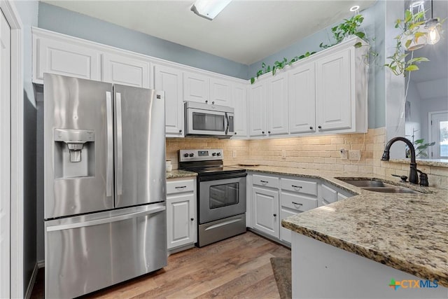 kitchen with hardwood / wood-style floors, sink, light stone countertops, white cabinetry, and stainless steel appliances