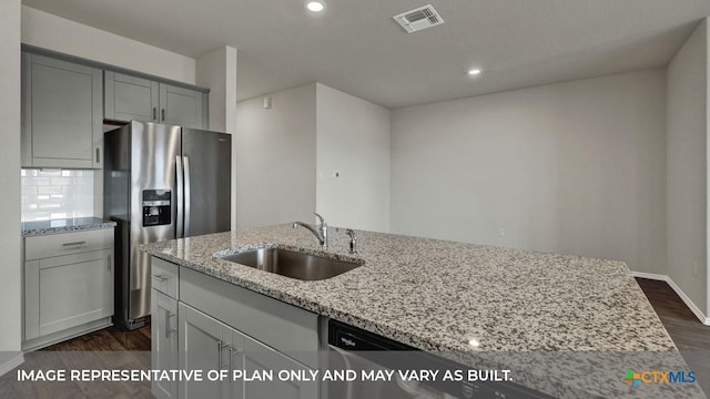 kitchen with stainless steel fridge, light stone counters, dark wood-style flooring, and a sink