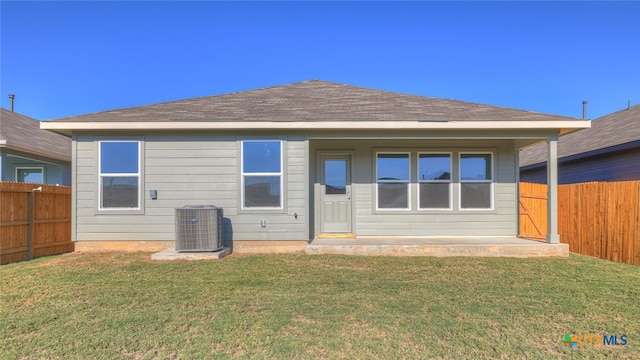 back of property with cooling unit, a fenced backyard, a yard, and roof with shingles