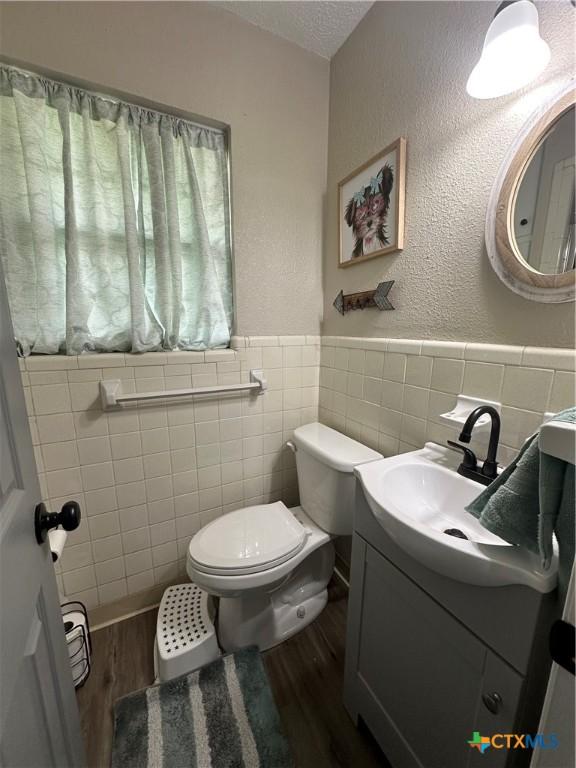 208 Old Fort Gates Rd, Gatesville, TX 76528 - half bath with tile walls, wood finished floors, toilet, wainscoting, and vanity