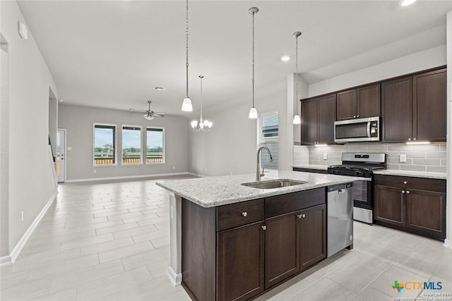 kitchen featuring sink, appliances with stainless steel finishes, light stone counters, tasteful backsplash, and an island with sink