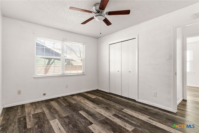 unfurnished bedroom featuring a closet, baseboards, a textured ceiling, and dark wood finished floors