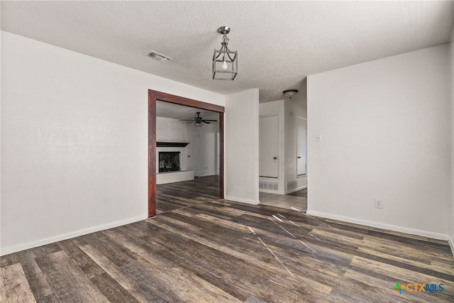 interior space with a textured ceiling, wood finished floors, visible vents, and a fireplace with raised hearth