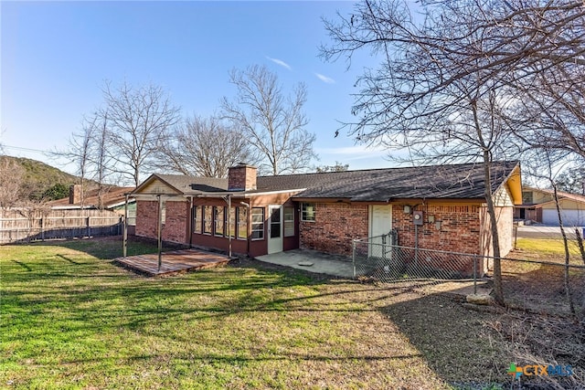 rear view of property featuring fence, a yard, a sunroom, brick siding, and a chimney