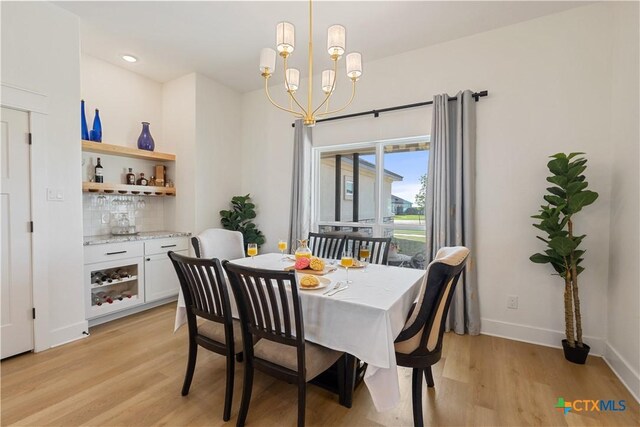 dining room featuring baseboards, a bar, a chandelier, and light wood-type flooring