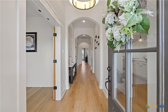 hall featuring light wood-type flooring, baseboards, arched walkways, and recessed lighting