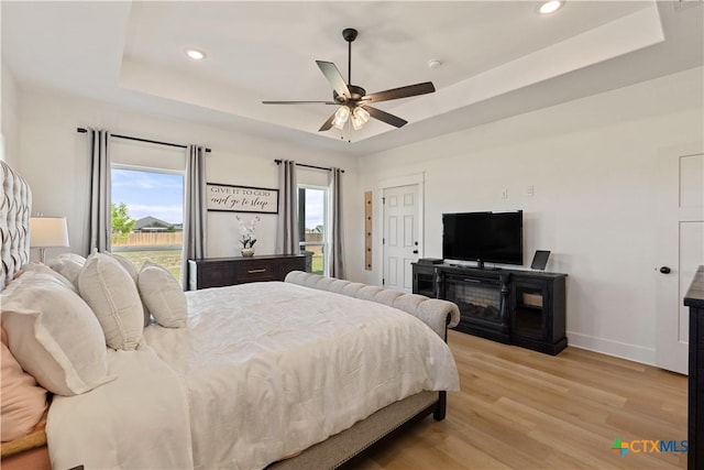 bedroom featuring a tray ceiling, light wood finished floors, multiple windows, and recessed lighting