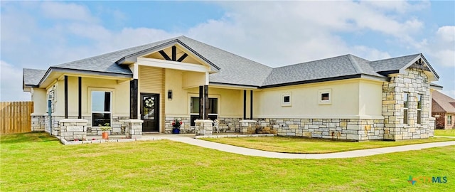 rear view of property with stucco siding, fence, stone siding, and a lawn