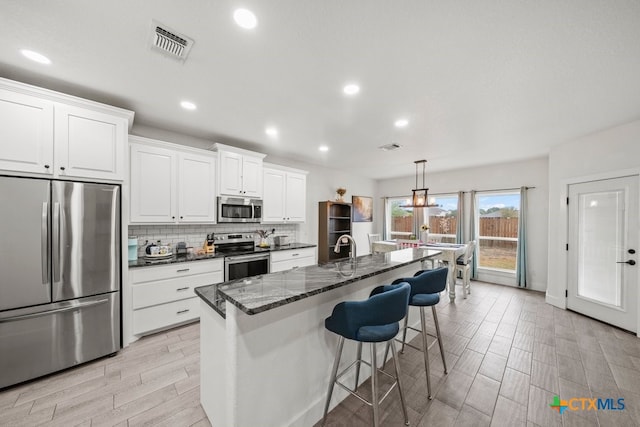 kitchen with hanging light fixtures, white cabinetry, an island with sink, and appliances with stainless steel finishes