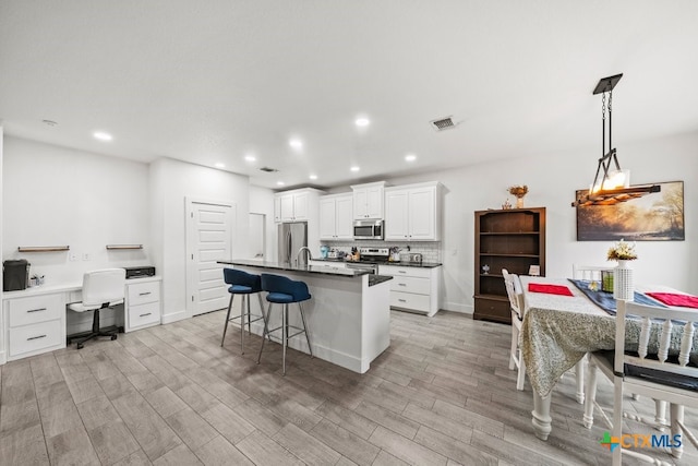 kitchen with white cabinetry, a kitchen bar, a center island with sink, appliances with stainless steel finishes, and light wood-type flooring