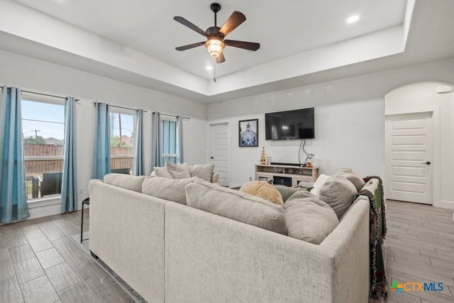 living room featuring wood-type flooring, a tray ceiling, and ceiling fan