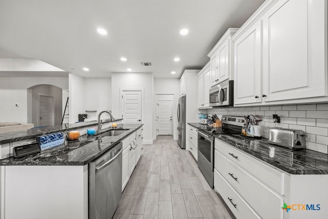 kitchen featuring white cabinetry, sink, light hardwood / wood-style flooring, dark stone countertops, and appliances with stainless steel finishes