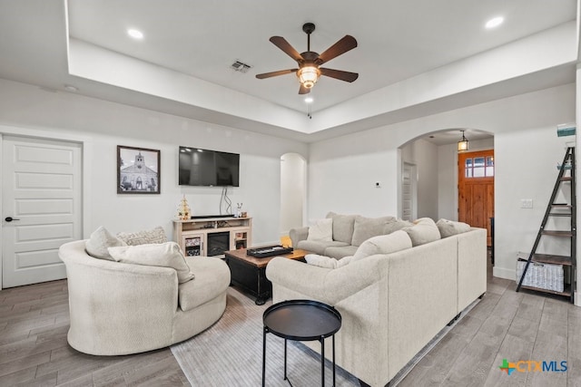 living room with a raised ceiling, a fireplace, ceiling fan, and light hardwood / wood-style flooring