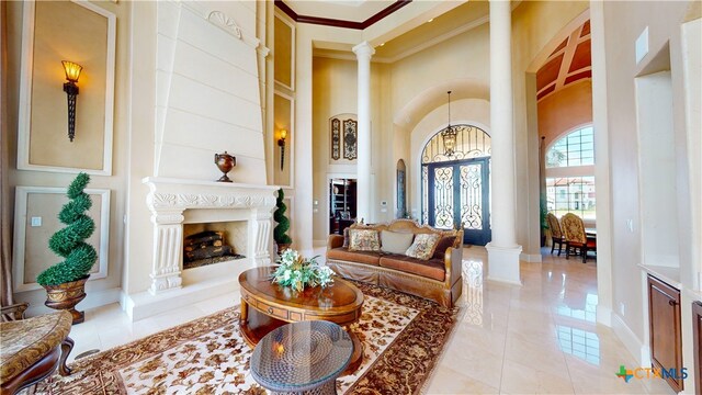 interior space featuring an inviting chandelier, a towering ceiling, decorative columns, ornamental molding, and a large fireplace