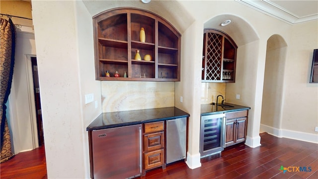 bar featuring stainless steel refrigerator, sink, ornamental molding, beverage cooler, and dark hardwood / wood-style flooring