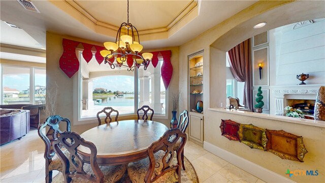 tiled dining room with a water view, a notable chandelier, crown molding, a tray ceiling, and built in features