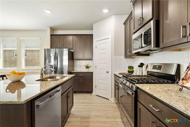 2917 Sage Ranch Dr, Leander, TX 78641 - kitchen with appliances with stainless steel finishes, dark brown cabinets, light wood finished floors, light stone countertops, and a center island with sink