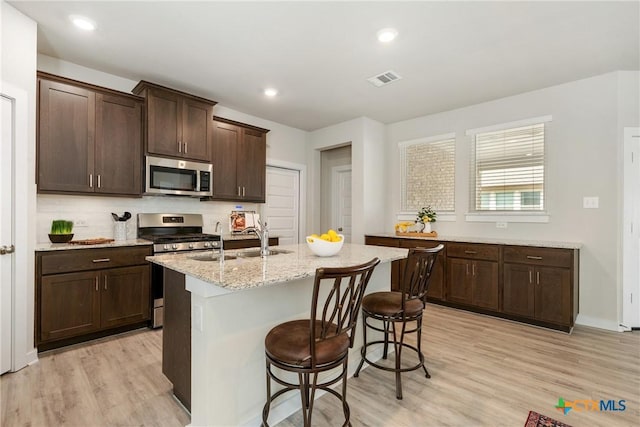 2917 Sage Ranch Dr, Leander, TX 78641 - kitchen with appliances with stainless steel finishes, light wood-type flooring, dark brown cabinetry, a kitchen island with sink, and a kitchen breakfast bar