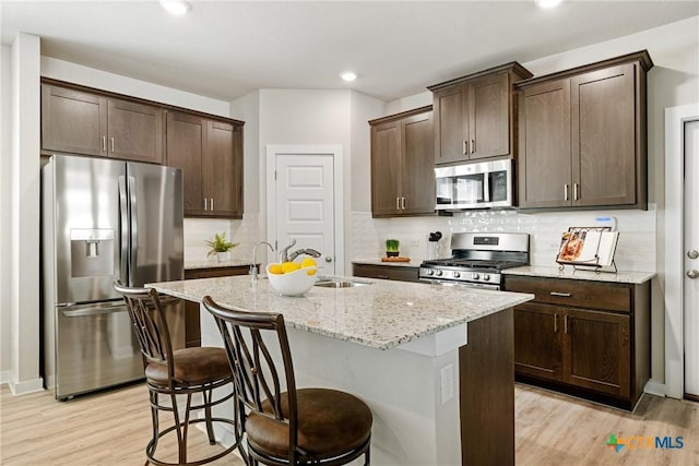 2917 Sage Ranch Dr, Leander, TX 78641 - kitchen with stainless steel appliances, dark brown cabinetry, light stone counters, light wood-style floors, and a kitchen island with sink