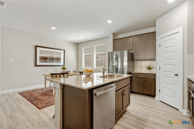 2917 Sage Ranch Dr, Leander, TX 78641 - kitchen with stainless steel appliances, light wood-style floors, light stone counters, an island with sink, and decorative backsplash