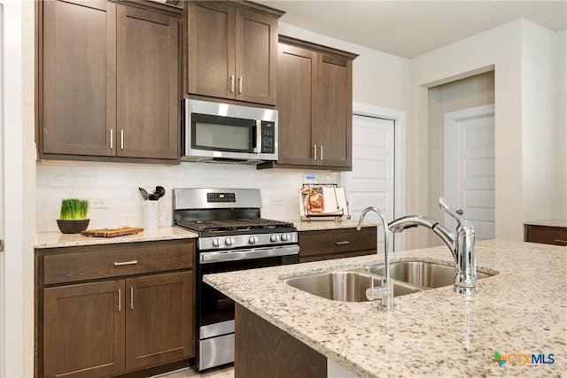 2917 Sage Ranch Dr, Leander, TX 78641 - kitchen with appliances with stainless steel finishes, backsplash, dark brown cabinetry, and light stone counters